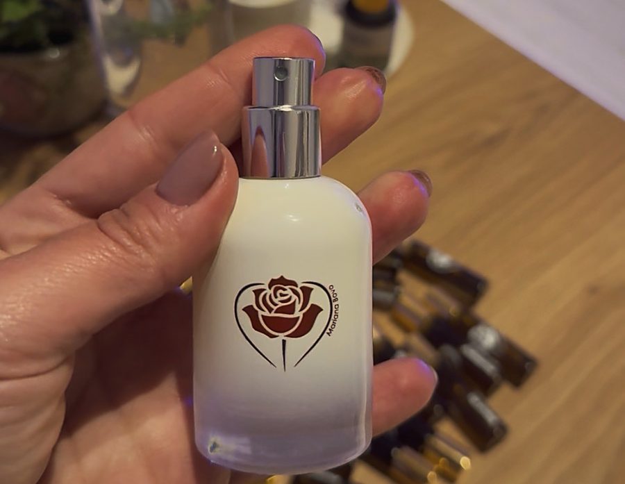 Mão segurando frasco spray branco com rosa vermelha estampada